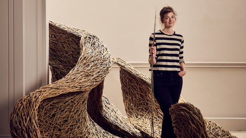 Woman holding willow stood indoors next to a large flowing willow sculpture